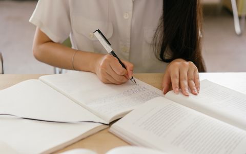 学习者对照打开的书本在笔记本上写字